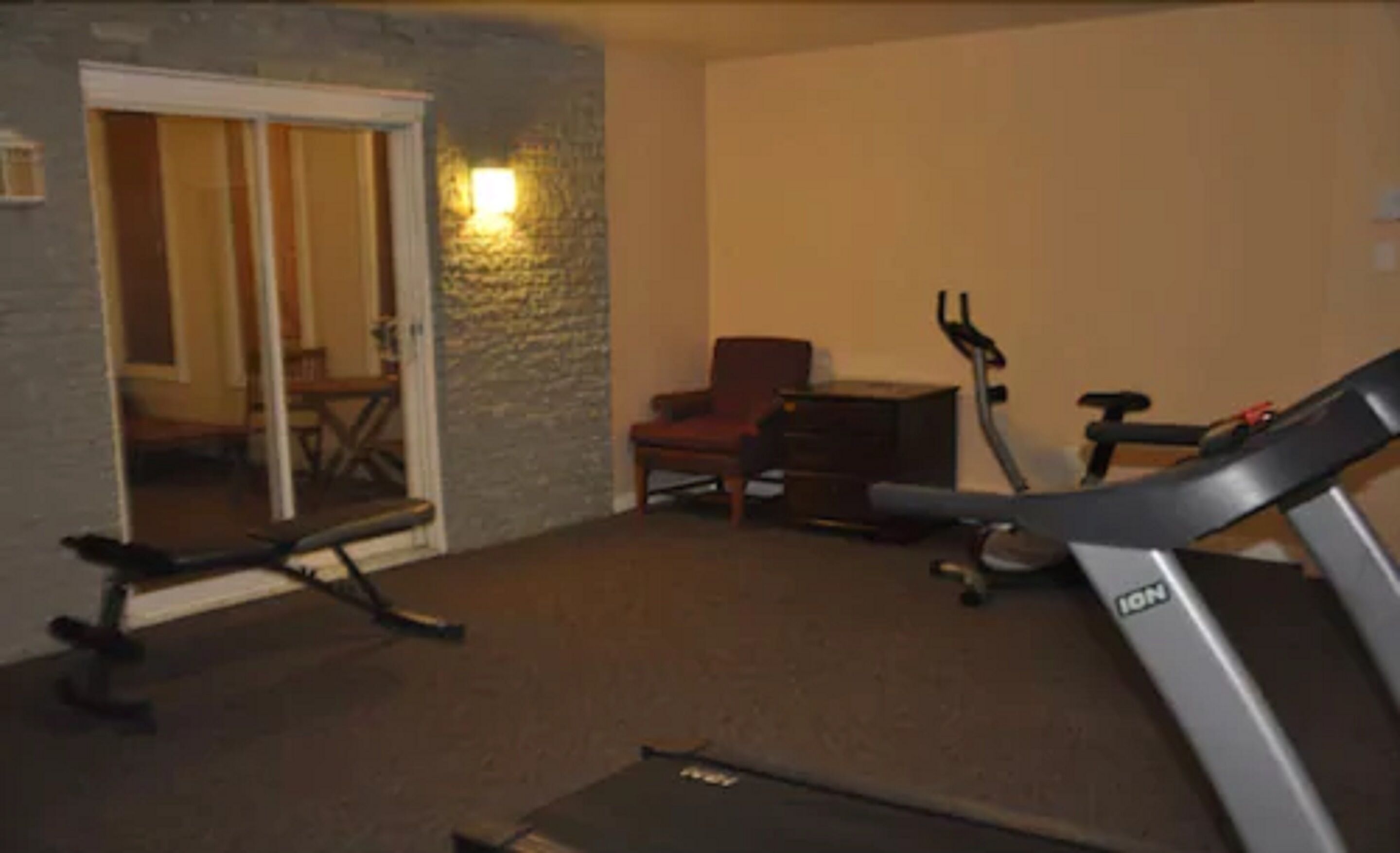 A room with a treadmill, a chair, and a desk.
