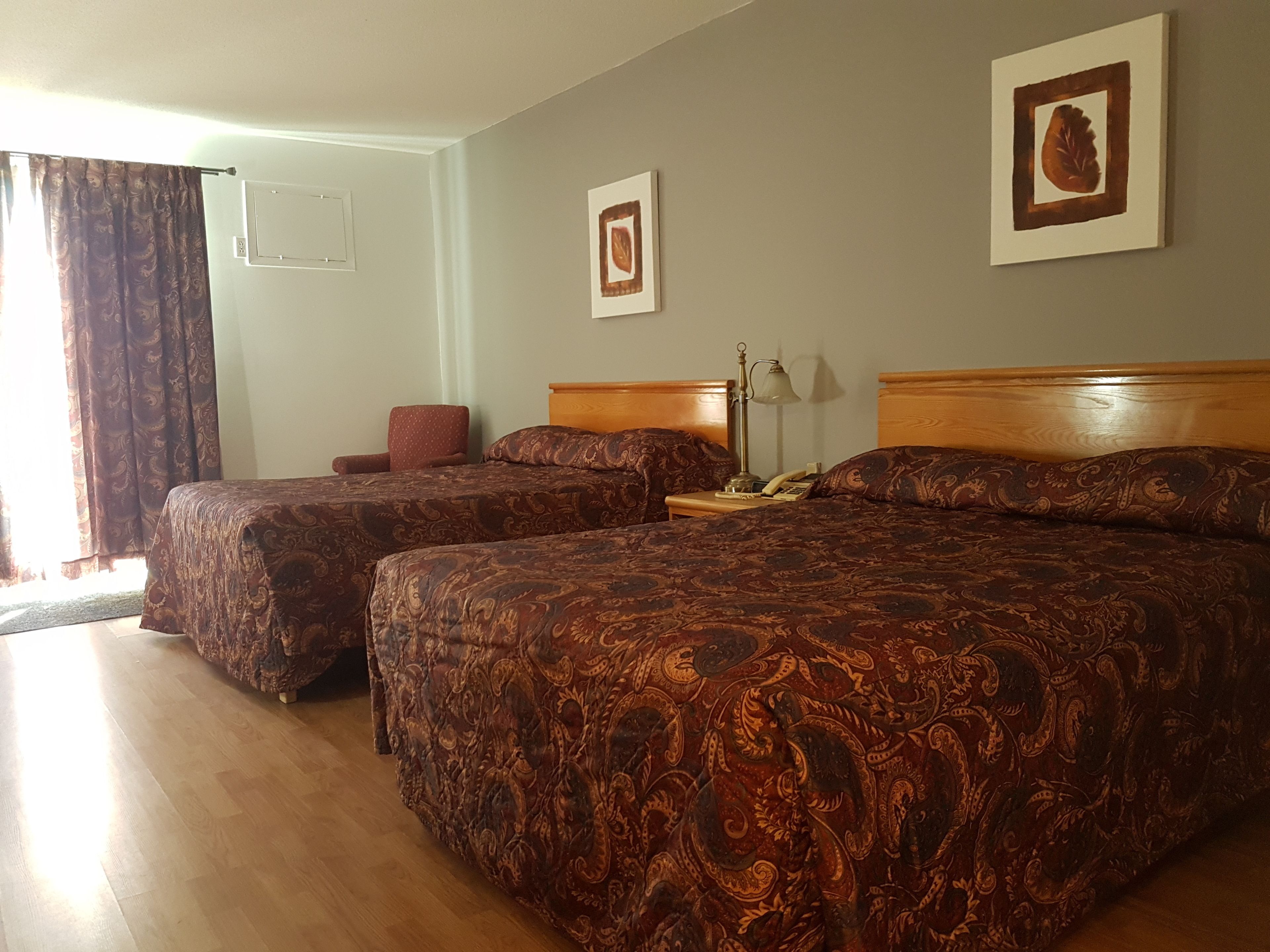 A hotel room with two beds, a chair, a nightstand with a lamp, and a framed picture on the wall.