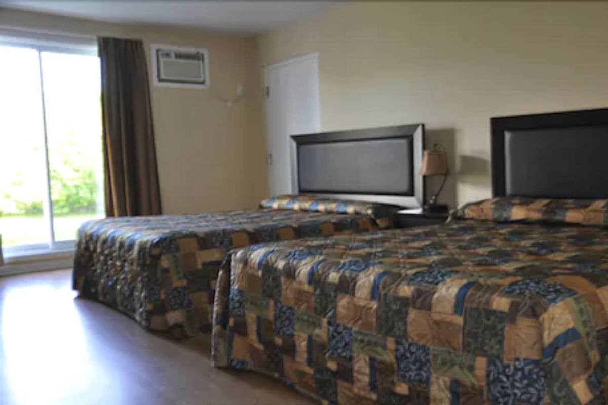Habitación de hotel con dos camas, televisor y ventana con cortinas.