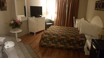A bedroom with a bed, a dresser, a television, a bathroom with a bathtub, and a window with curtains.
