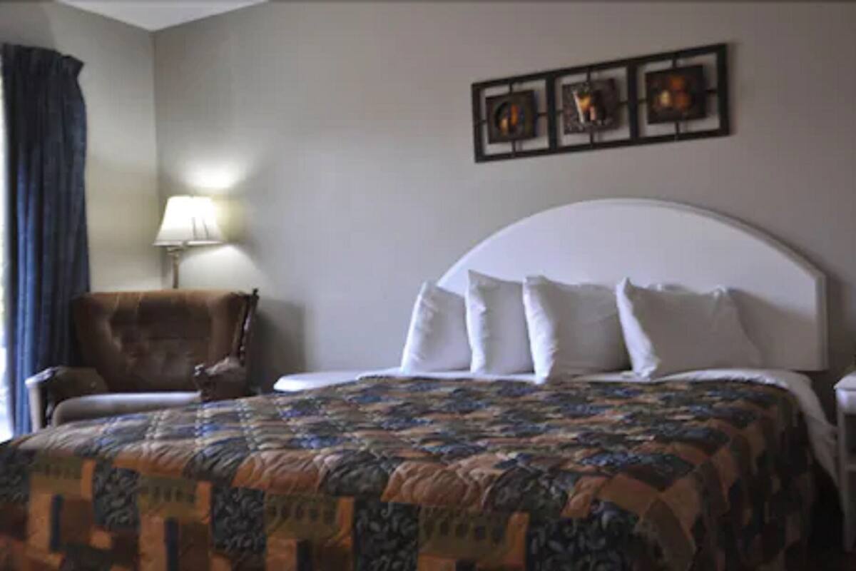 Una habitación de hotel con una cama grande, una silla, una lámpara y una obra de arte en la pared.