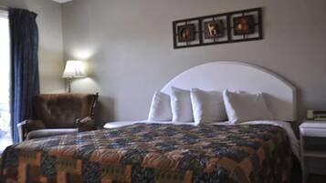 A hotel room with a large bed, a chair, a lamp, and artwork on the wall.