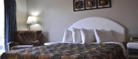 Una habitación de hotel con una cama grande, una silla, una lámpara y una obra de arte en la pared.