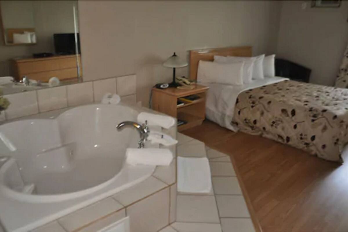 Una habitación de hotel con una bañera grande, una mesita de noche de madera, una cama con edredón floral y un espejo en la pared.