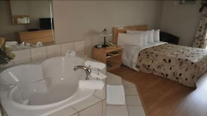 Una habitación de hotel con una bañera grande, una mesita de noche de madera, una cama con edredón floral y un espejo en la pared.