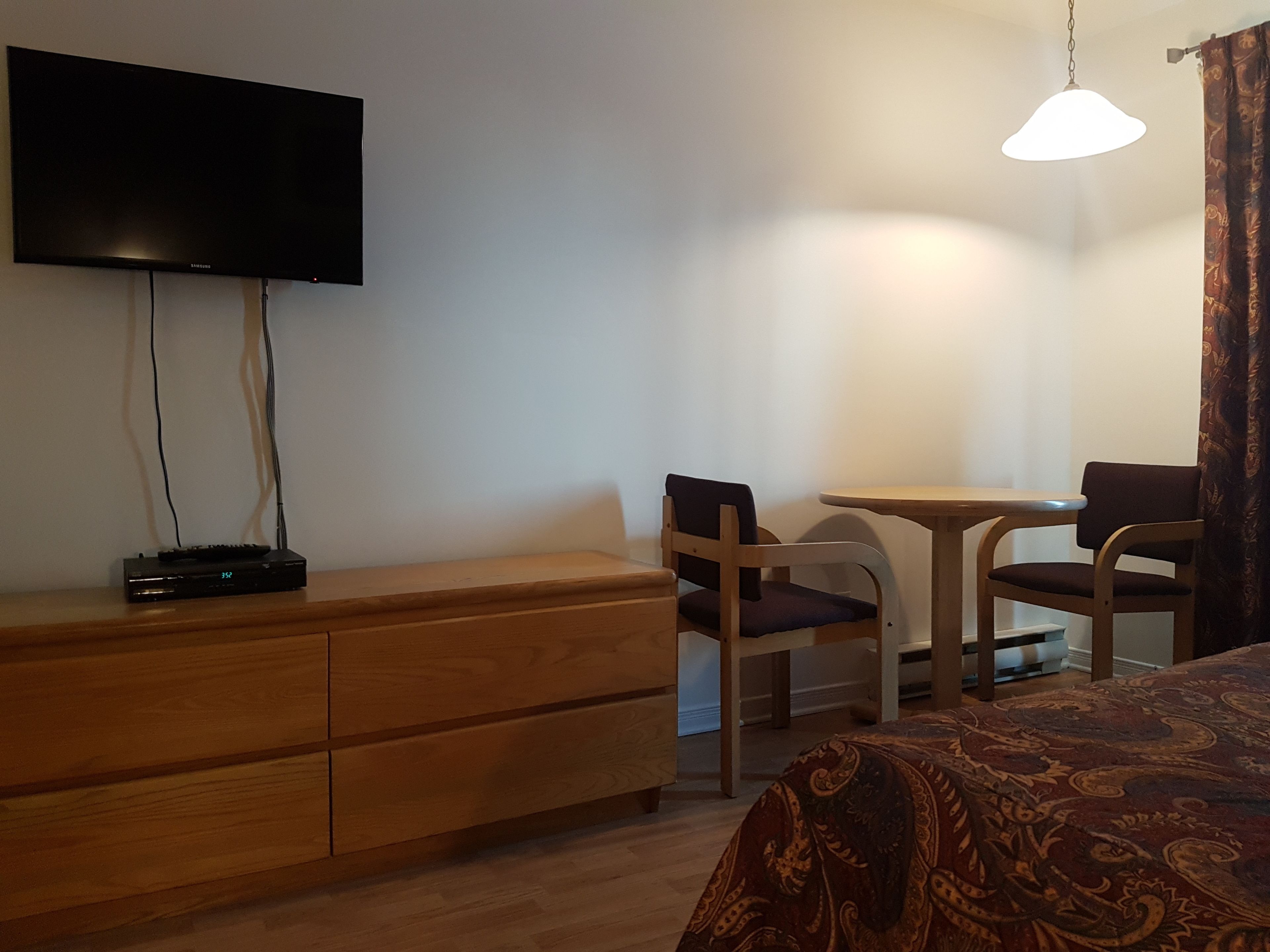 Una habitación de hotel con cama, escritorio, dos sillas, televisión y lámpara.