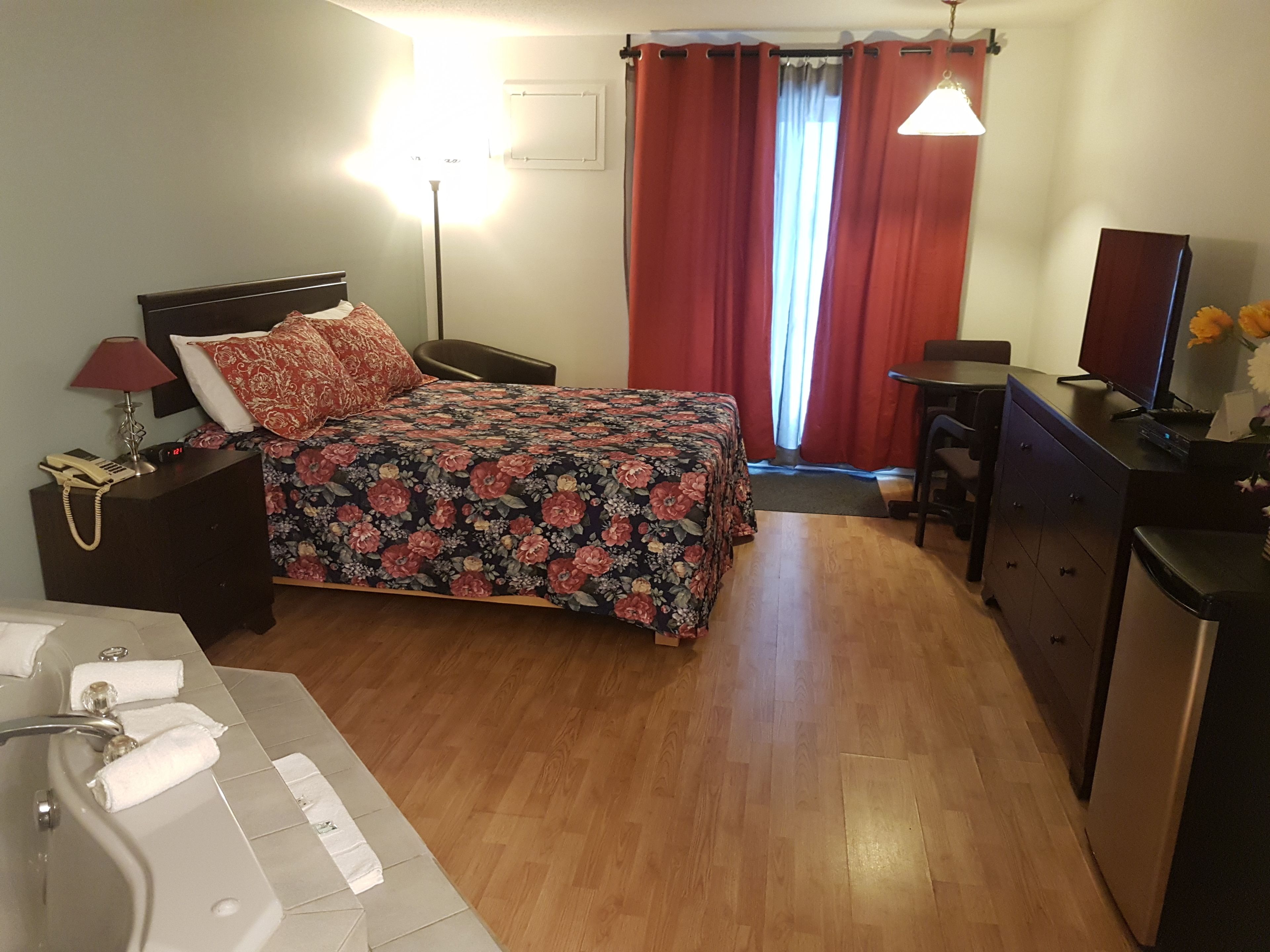 Habitación de hotel con cama, escritorio, silla, lámpara de escritorio, teléfono, televisión y baño con lavamanos y perchero para toallas.