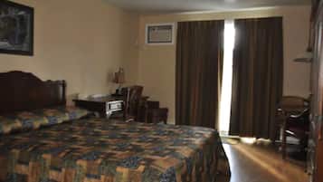 A hotel room with a large bed, a desk with a chair, a window with curtains, and a door.