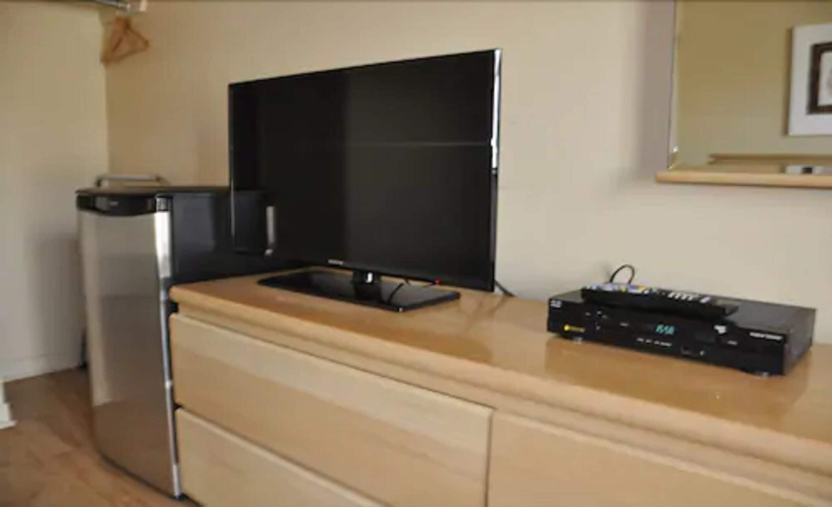 A kitchen with a black refrigerator, a black microwave, a black flat-screen TV, and a black entertainment unit with electronic devices.