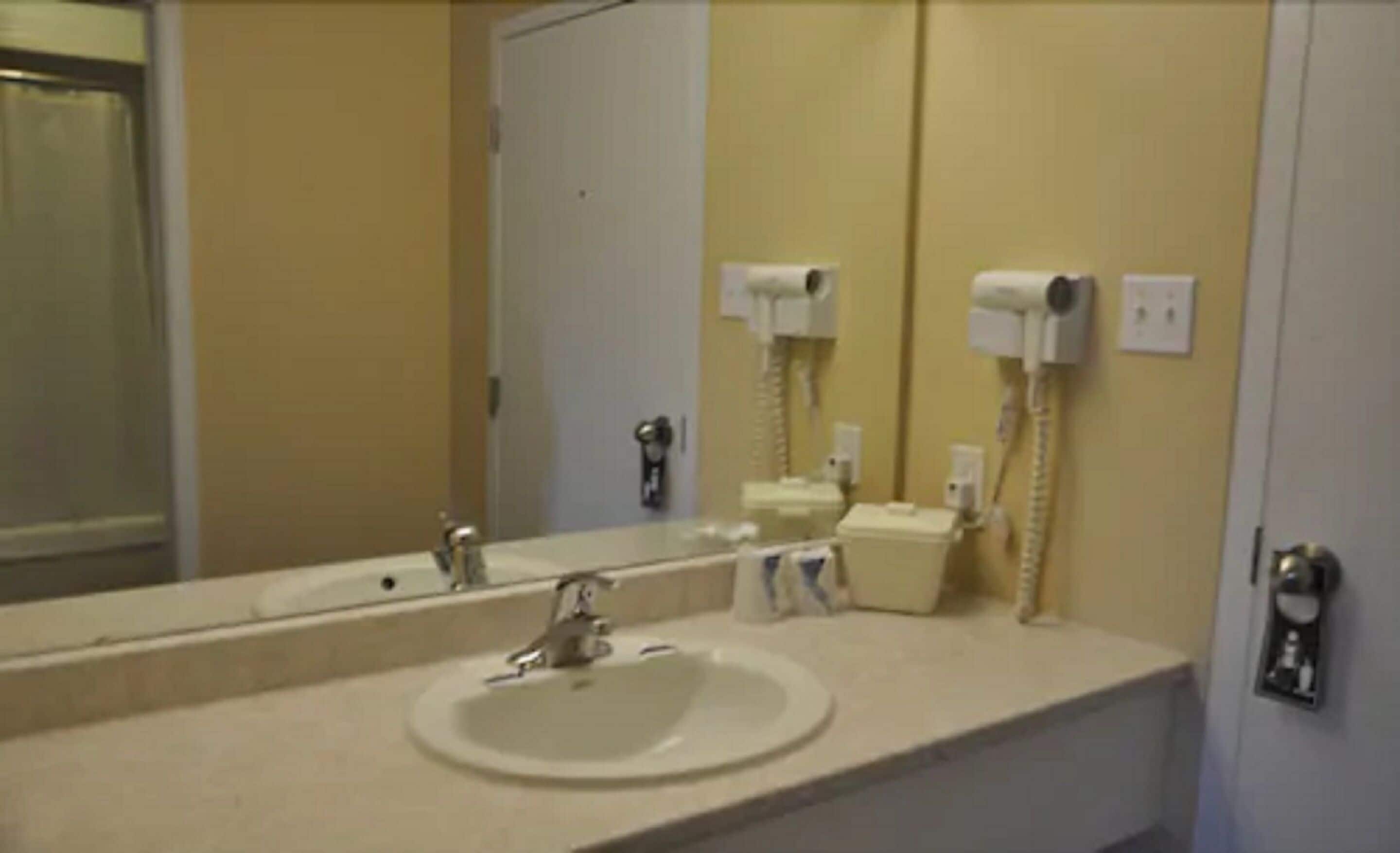 Un bagno con lavandino, specchio e due asciugacapelli fissati alla parete.