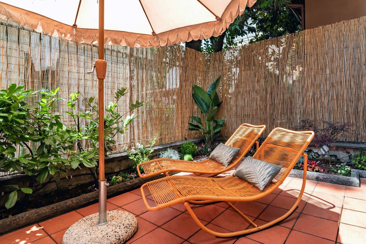 A patio area with two wicker lounge chairs, a round table, and a bamboo fence.