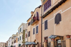 A row of traditional buildings with balconies and shutters, a sign indicating a hotel, and a gate with a number. - España (Rome)