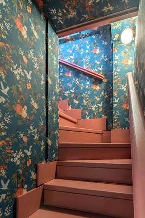 Una escalera con un fondo de papel tapiz floral y un espejo circular en la parte superior.