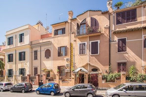 A row of Mediterranean-style buildings with balconies, a street, and parked cars. - España (Rome)