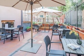 An outdoor patio area with tables and chairs, umbrellas, and potted plants. - España (Rome)