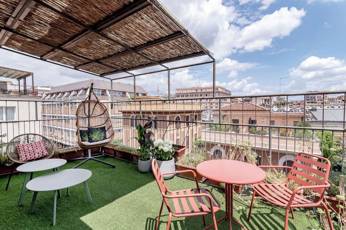 A rooftop terrace with a thatched roof, outdoor seating, and potted plants.