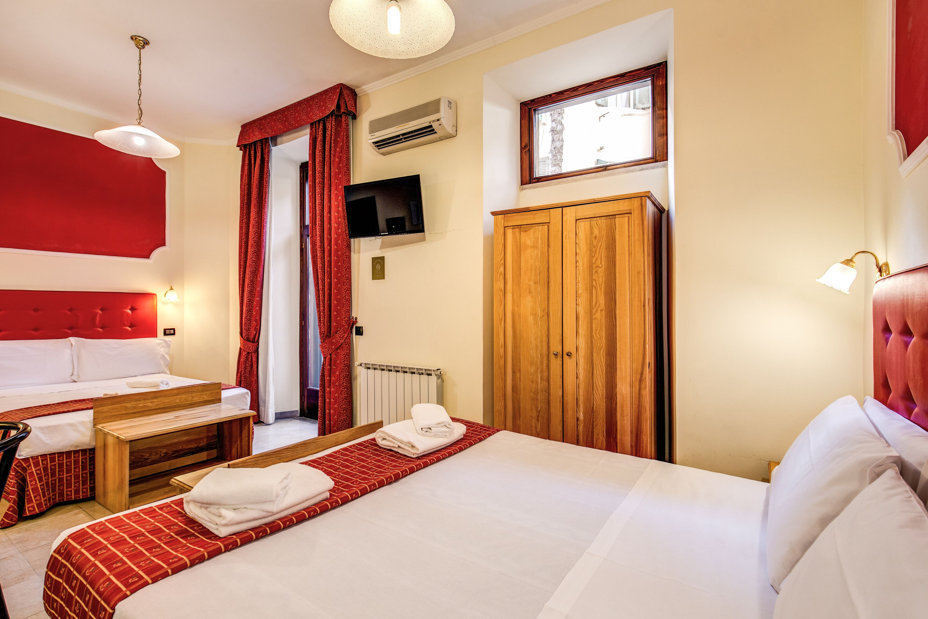 Ein Hotelzimmer mit einem großen Bett, einem kleineren Bett, einem Holzschrank, einem Fernseher und einem Fenster mit Blick.