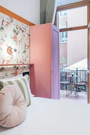 A bedroom with a bed, a pink wardrobe, a floral wallpaper, and a balcony with chairs and a table. - España (Rome)