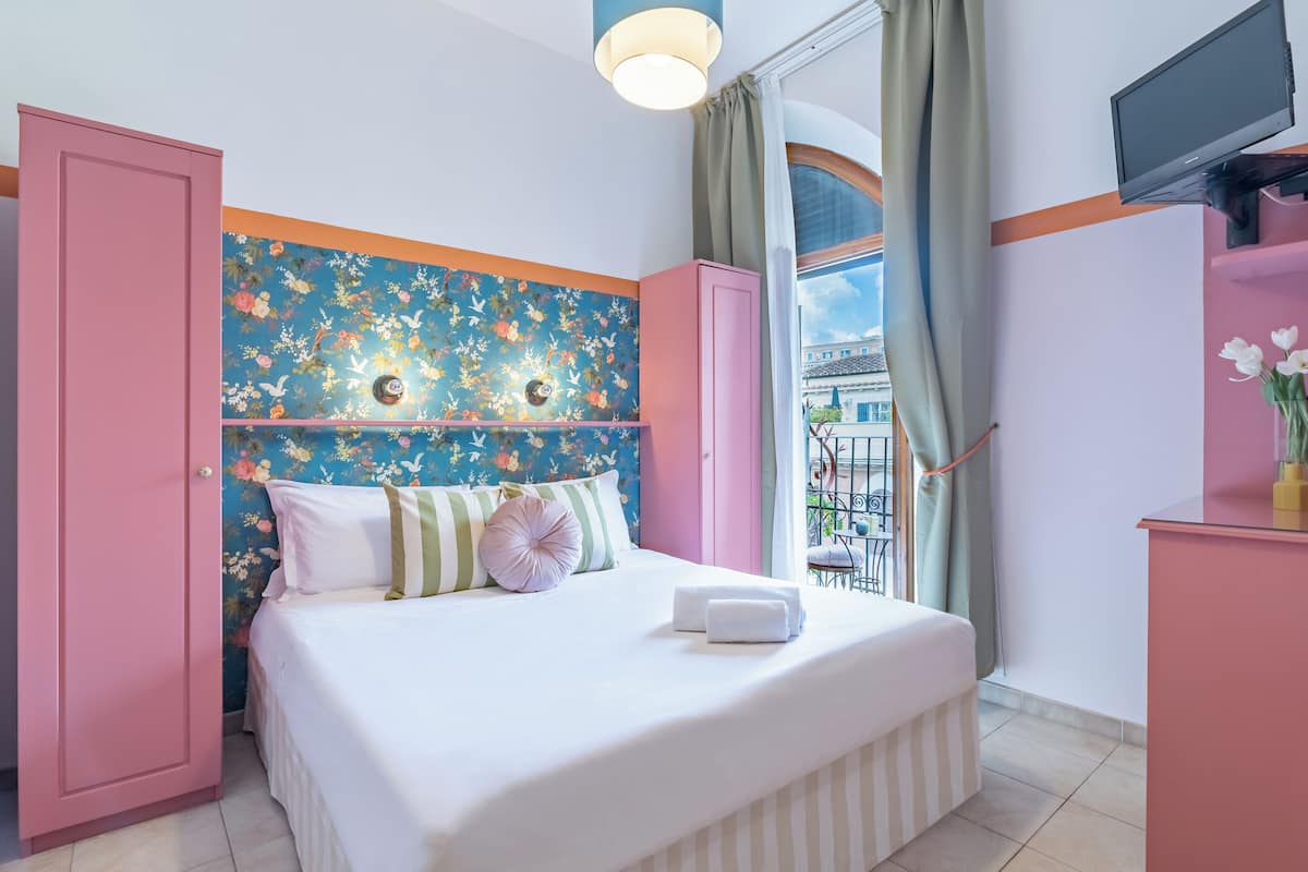 A bedroom with a bed, pink wardrobe, and a TV on a stand.