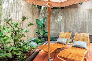 Un patio con dos sillones de mimbre, una valla de bambú y diversas plantas.