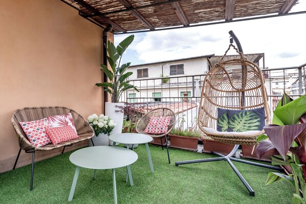 A balcony with wicker furniture, a hanging chair, and potted plants. - España (Rome)