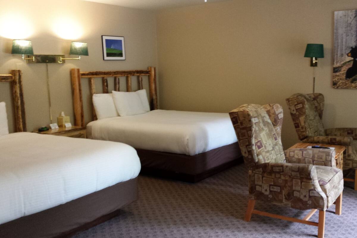 Habitación de hotel con dos camas, un cabecero de madera, un sillón estampado y un cuadro en la pared.