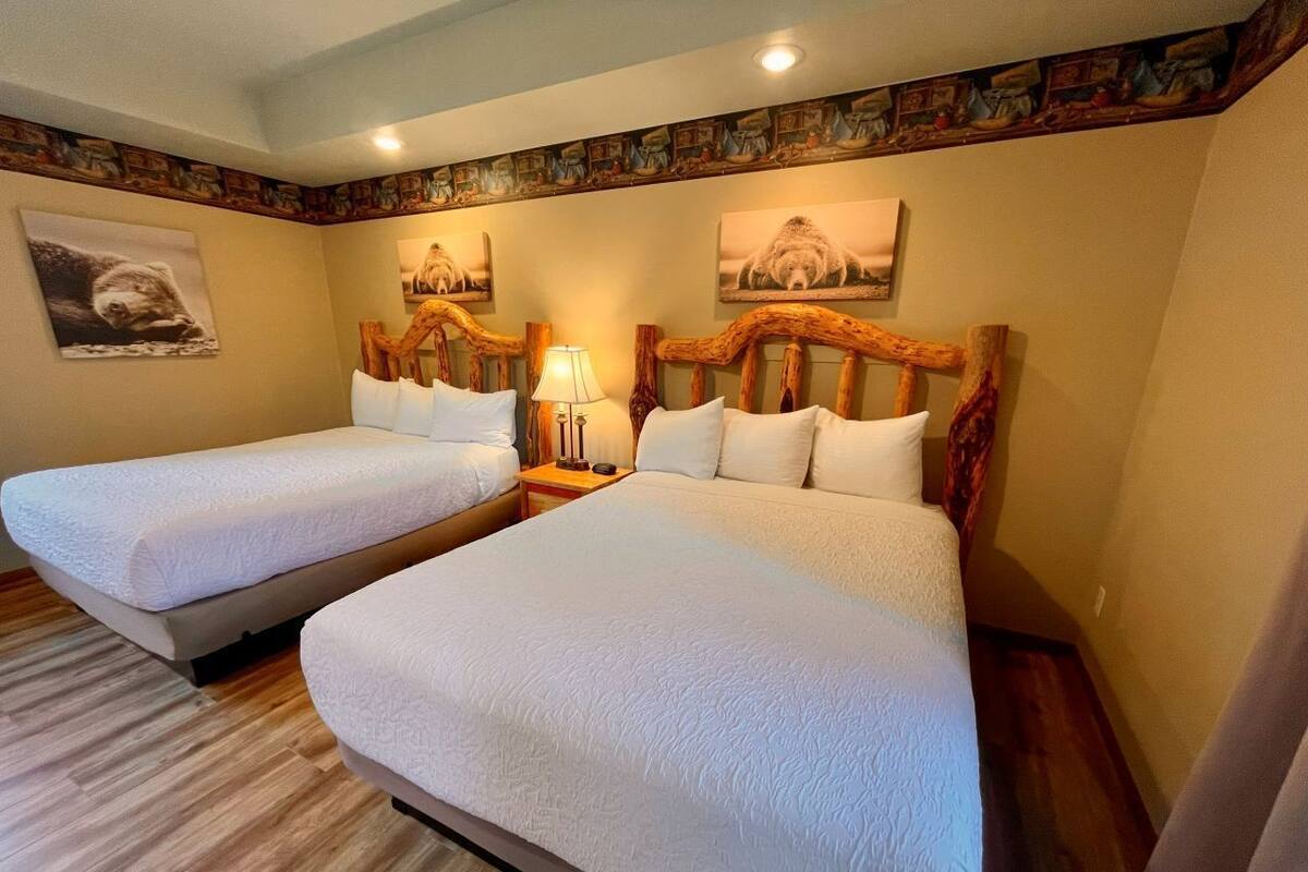 Habitación de hotel con dos camas, cabeceros de madera, una mesita de noche con lámpara y un cuadro en la pared.