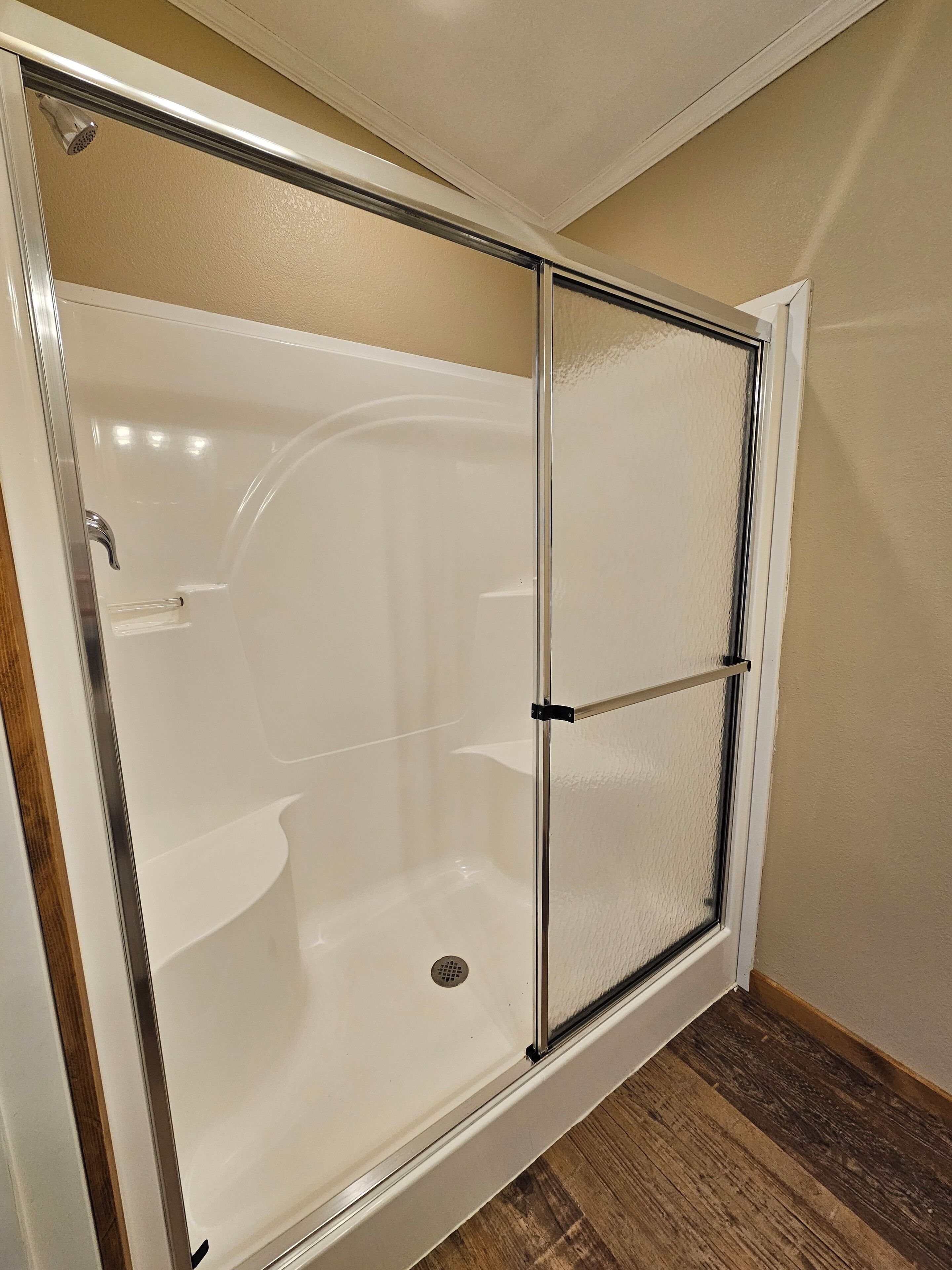 Una cabina de ducha con paredes de vidrio, una bañera blanca, un cabezal de ducha y desagüe.