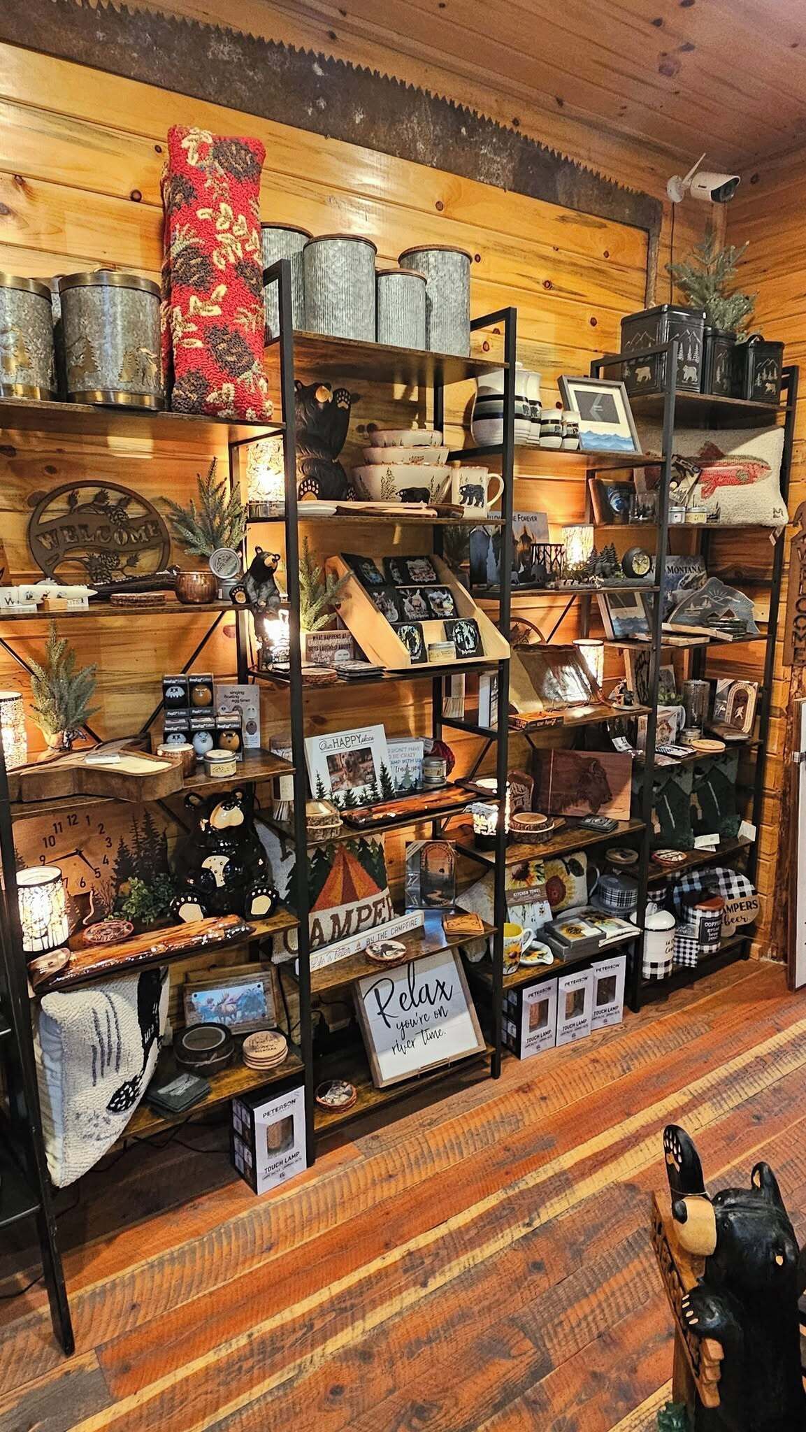 A rustic cabin interior with wooden walls and shelves displaying camping gear, mugs, and decorative items.