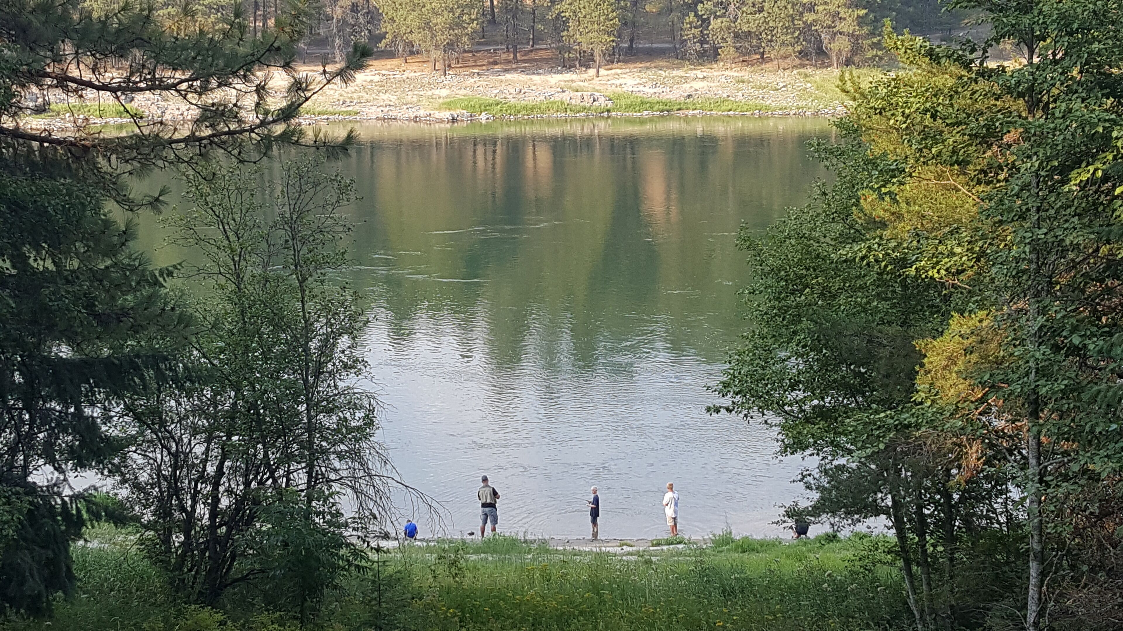A lake with people fishing, surrounded by trees and a grassy area.