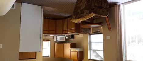 A compact kitchen with wooden cabinets, a microwave, and a small refrigerator.