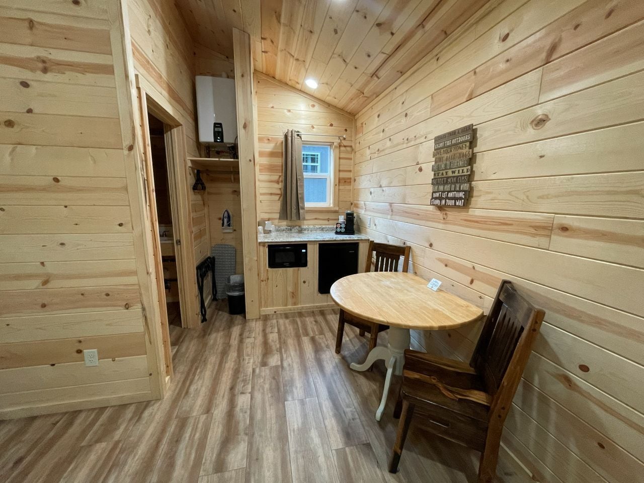 Ein Holzblockhaus-Interieur mit Esstisch und Stühlen, einer Küchenzeile mit Fenster sowie einem Holzboden.
