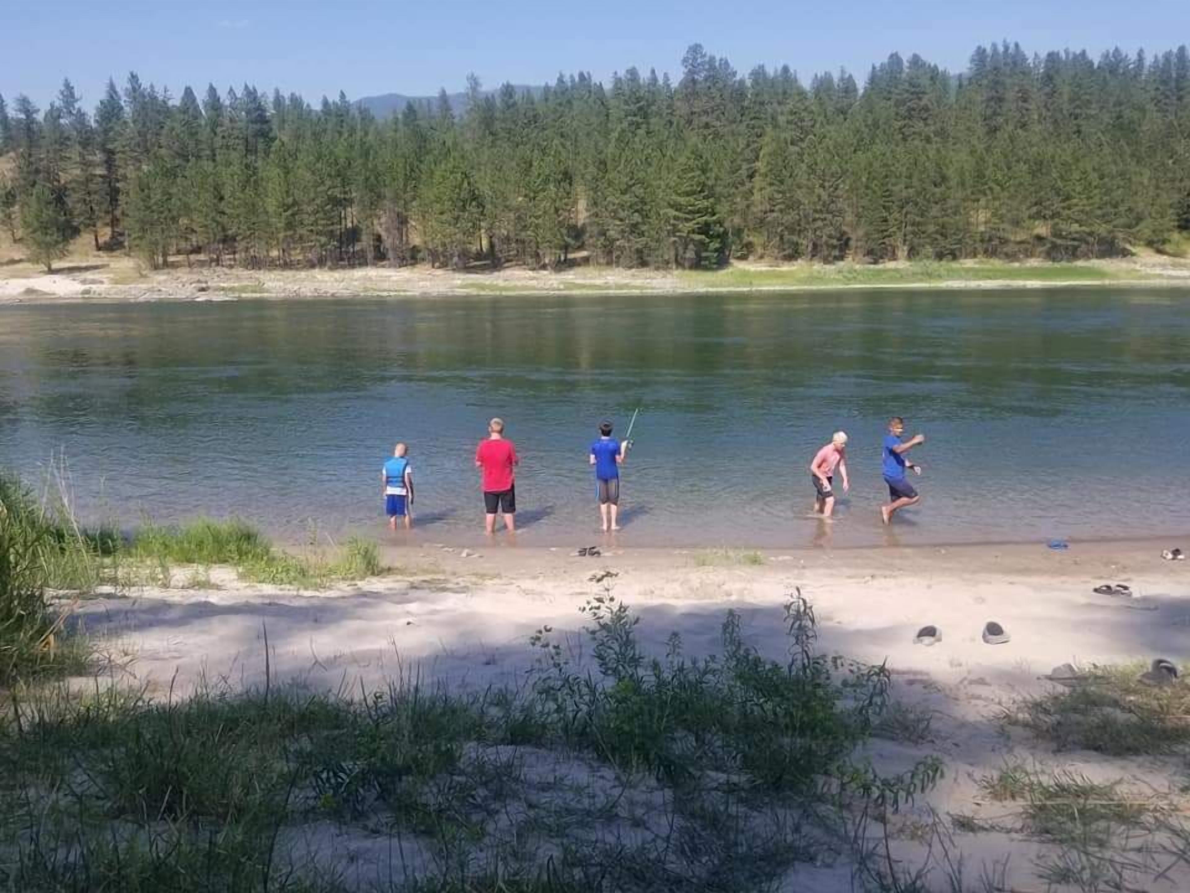 Un groupe de personnes se trouve au bord d’un lac, avec une forêt en arrière-plan.