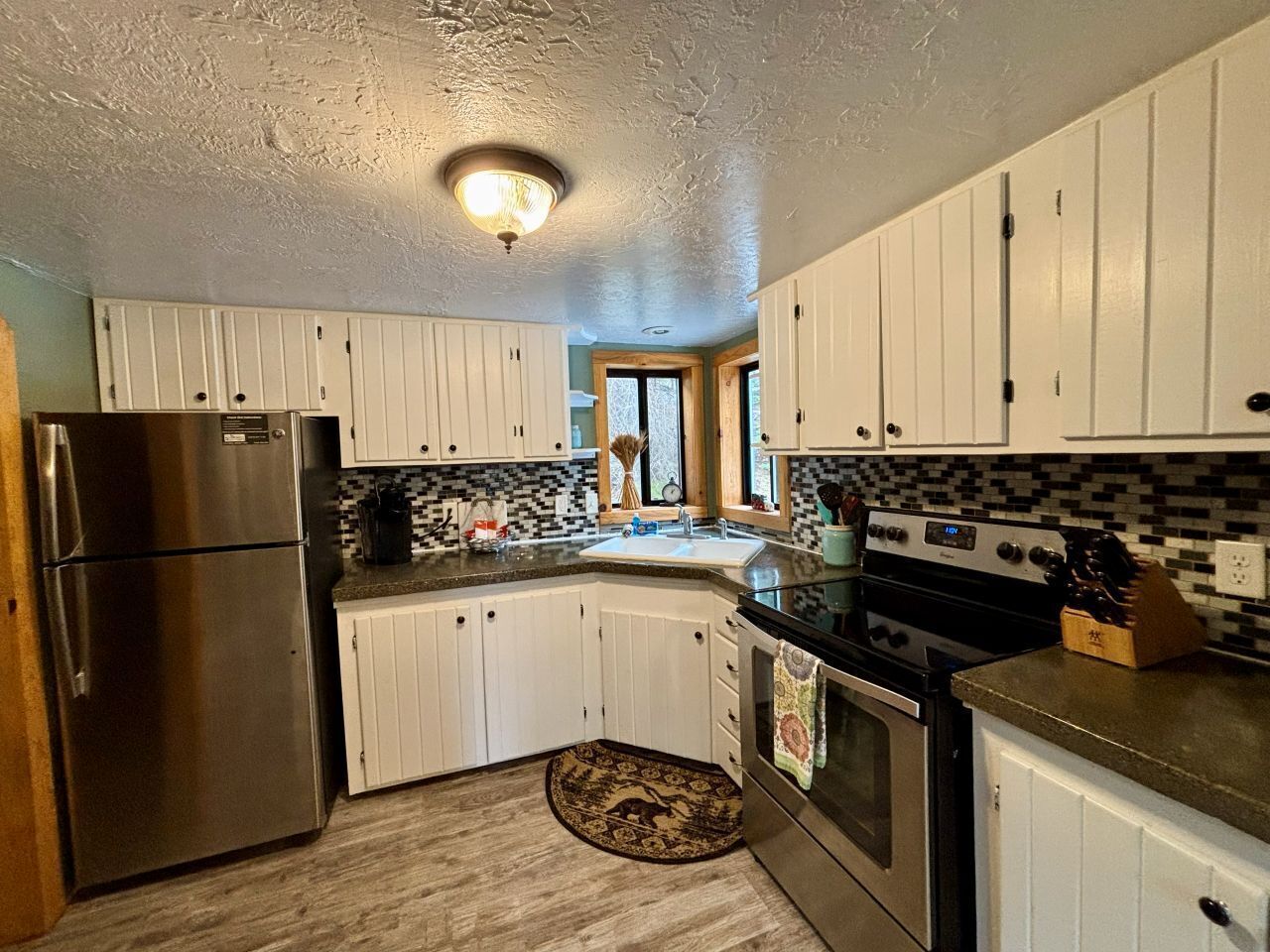 Una cocina con armarios blancos, un refrigerador de acero inoxidable, una estufa negra y un salpicadero de azulejos.