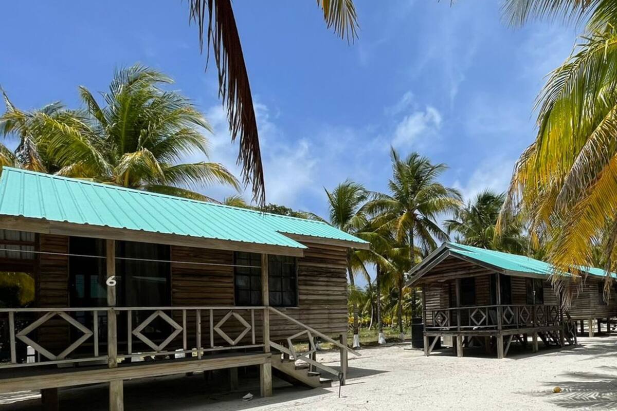 Un complejo turístico frente a la playa con cabañas de madera, cada una con balcón y techo de metal.