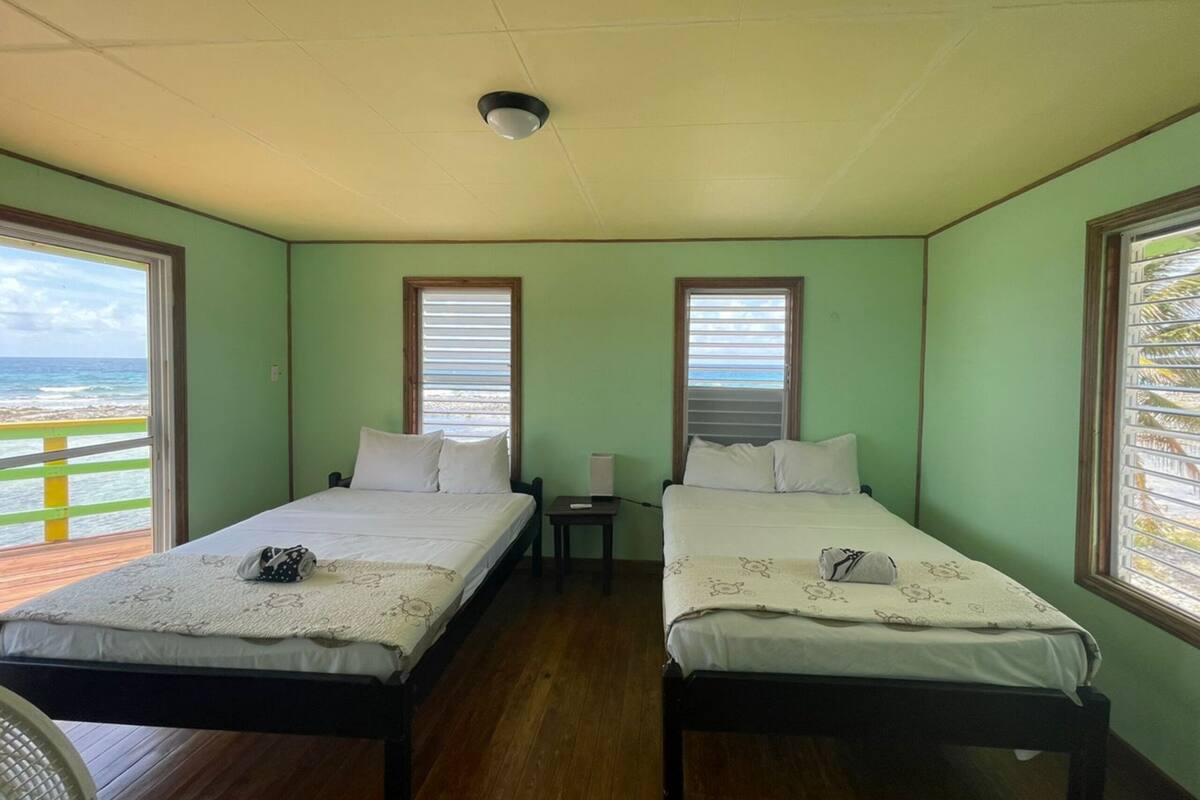 Una habitación con dos camas, un ventilador de techo y una ventana con vista al océano.