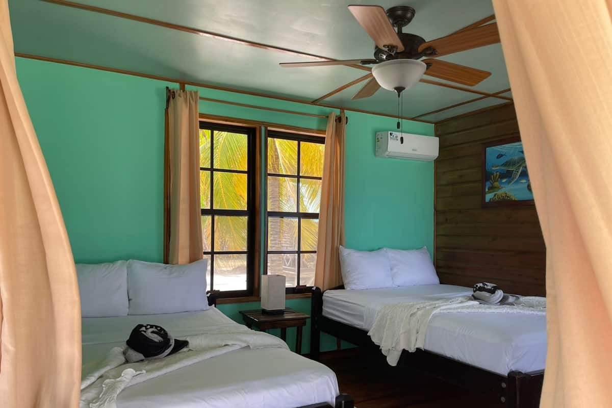 Una habitación con dos camas, ventilador de techo y ventana con cortinas.