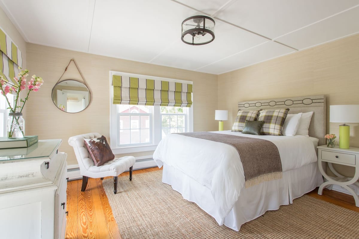 Une chambre à coucher avec un grand lit, une chaise, une commode, un miroir et une fenêtre avec des rideaux verts.