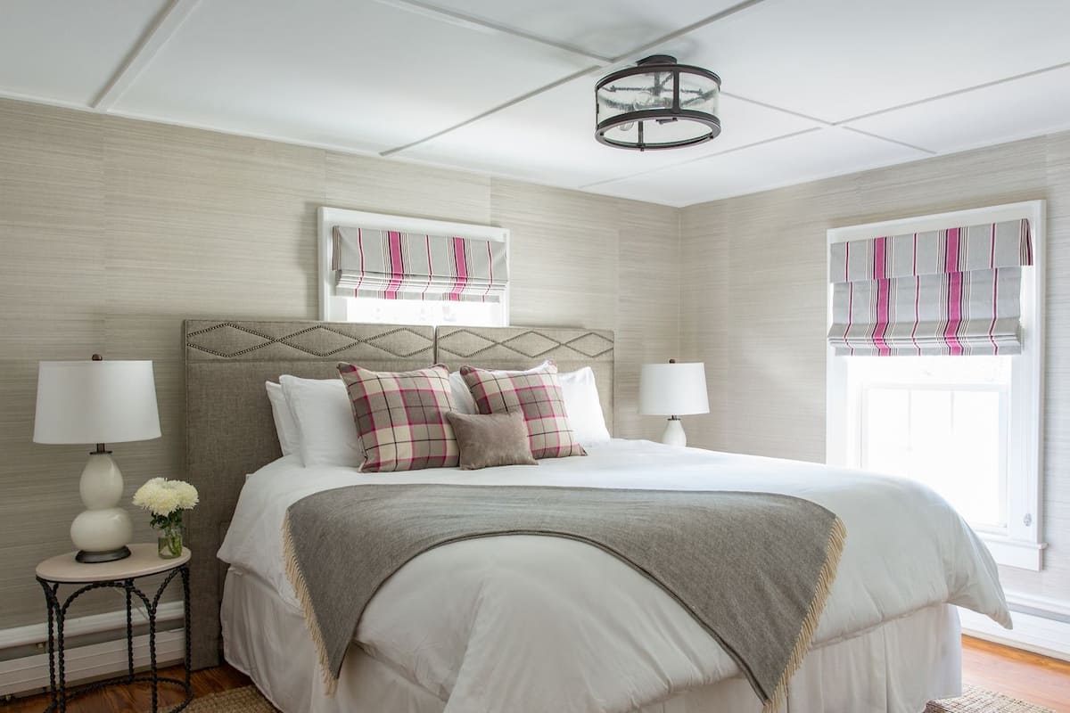 Une chambre à coucher bien aménagée, avec un grand lit, deux tables de chevet avec des lampes, une tête de lit décorative et une fenêtre avec des rideaux.