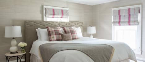Un dormitorio ordenado con una cama grande, dos mesitas de noche con lámparas, un cabecero decorativo y una ventana con cortinas.