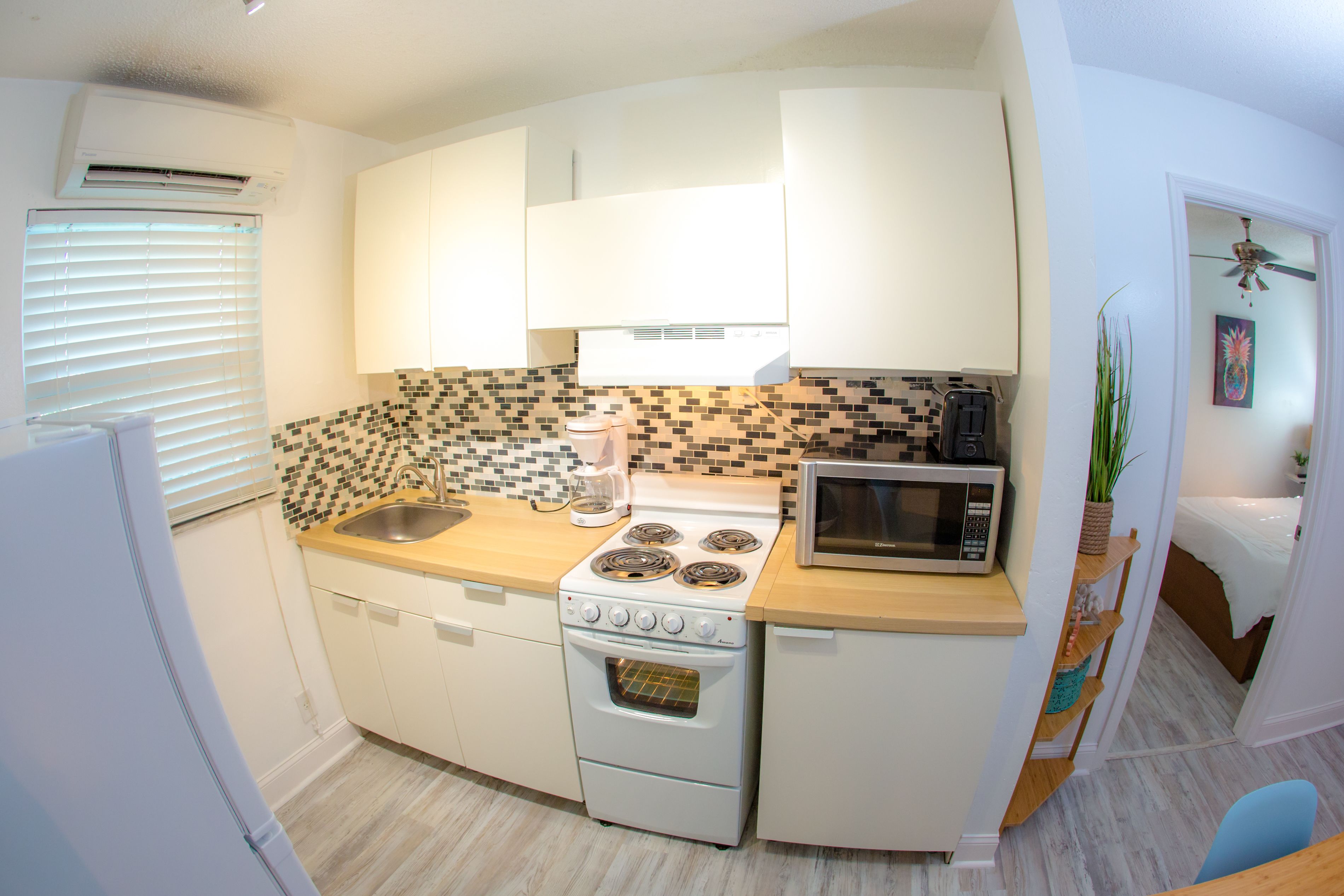 A compact kitchen with white cabinets, a stove, a microwave, and a sink.
