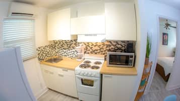 Una cocina funcional con gabinetes blancos, estufa, microondas y lavabo.