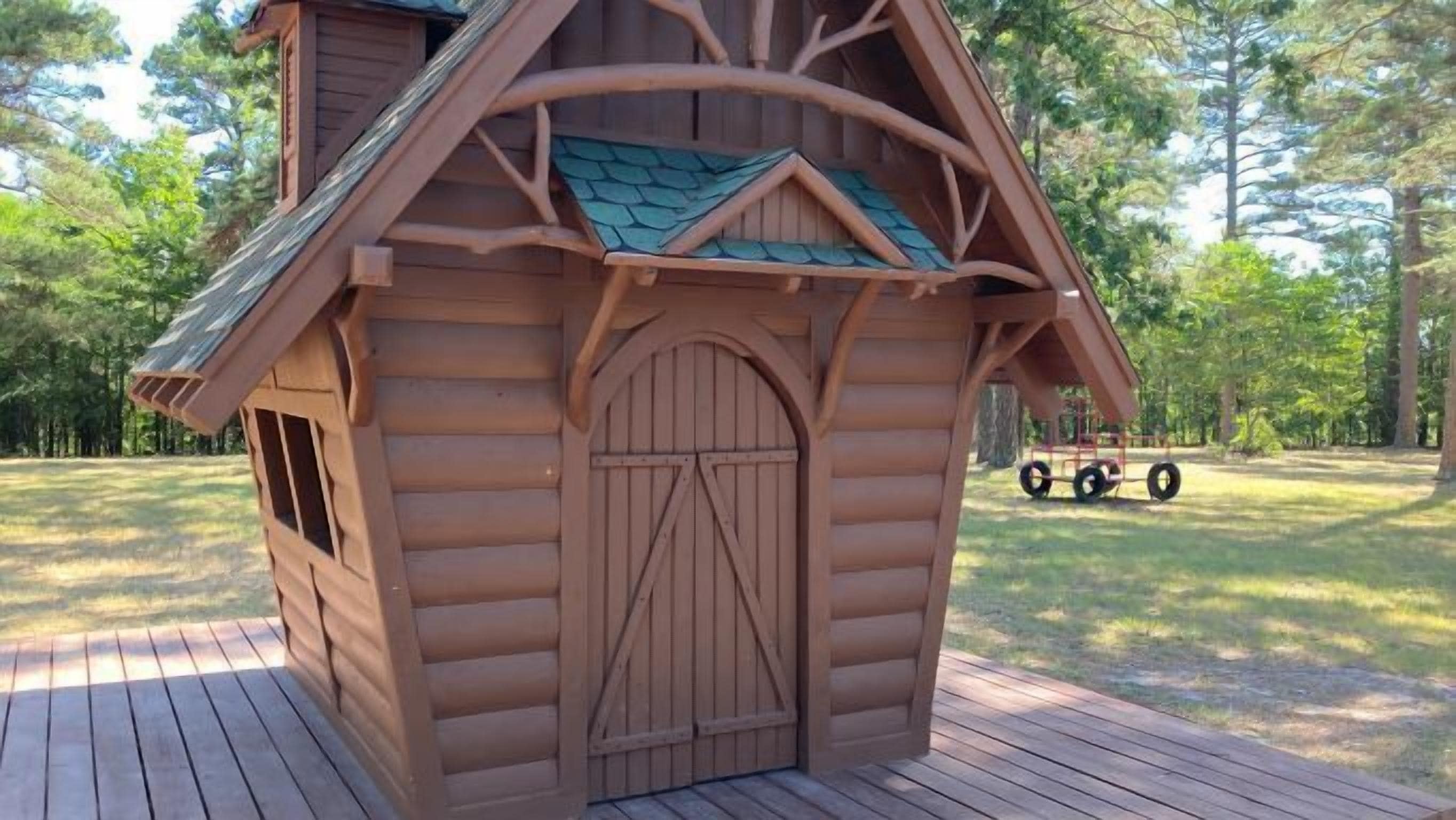 A wooden cabin with a pitched roof and a large arched door.