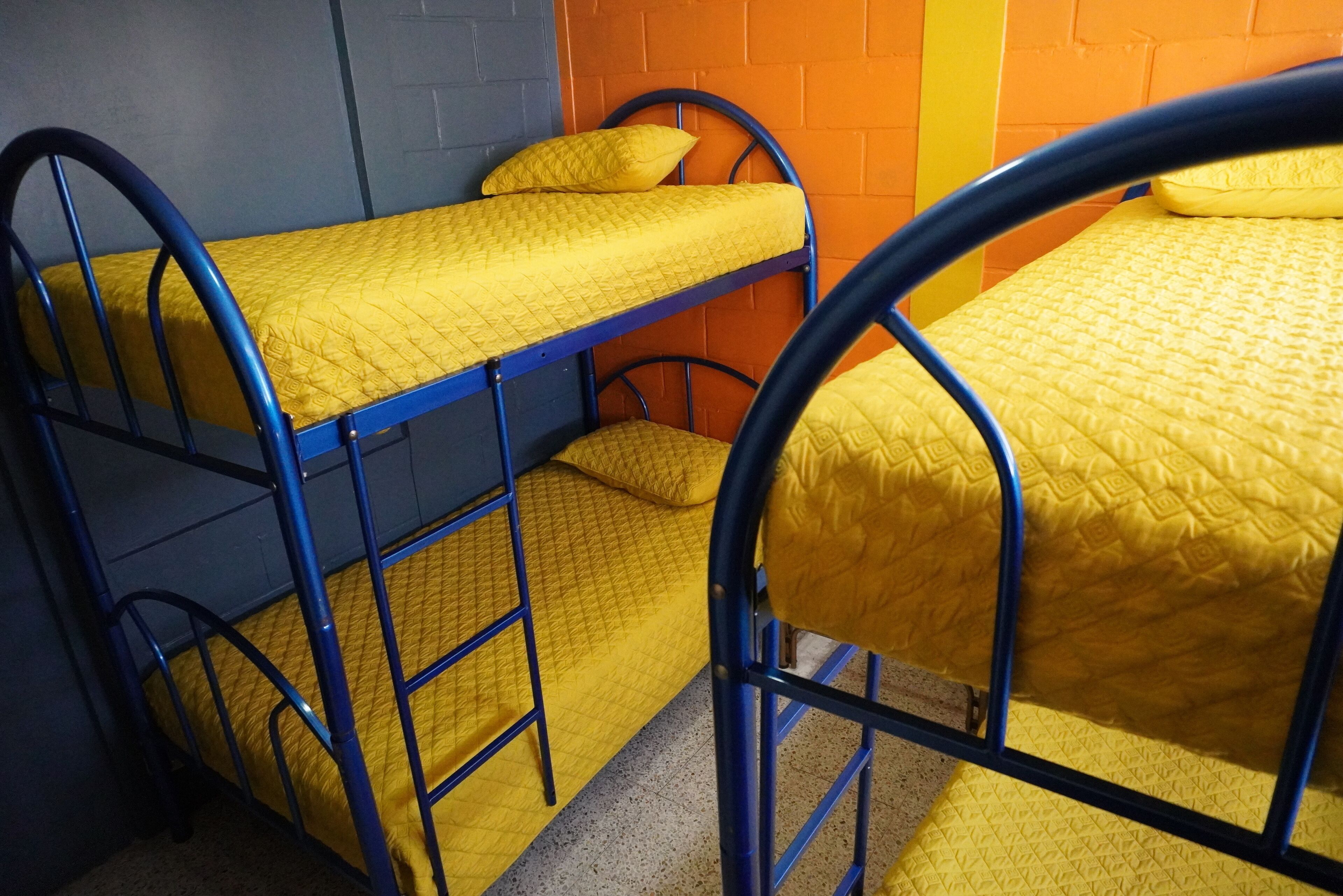 Bunk beds with yellow bedding and metal frames, arranged against a wall with a brick pattern.