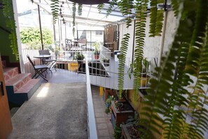 Ein überdachter Außenbereich mit Sitzgelegenheiten, Blumentöpfen und einer Treppe zu einer erhöhten Ebene.