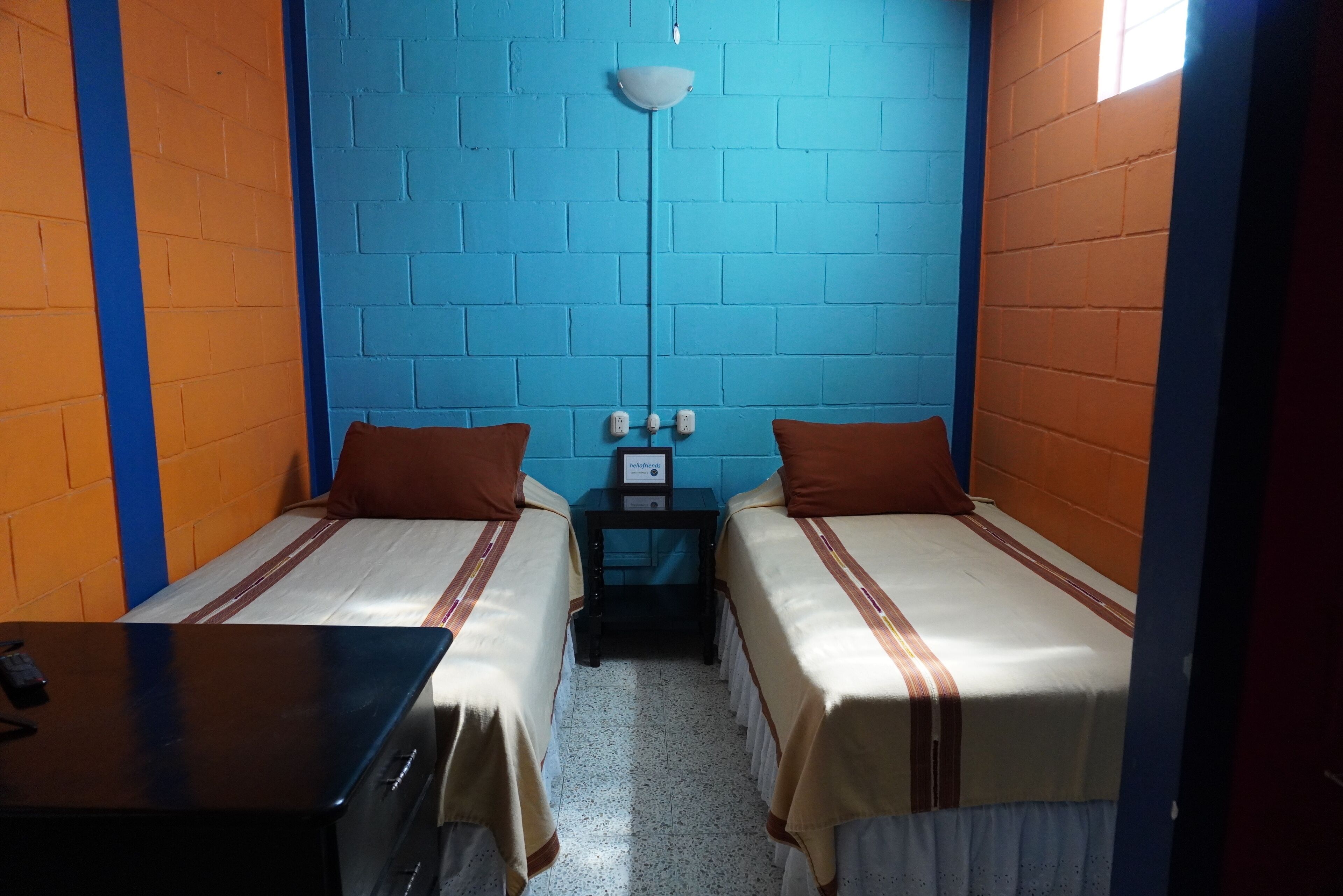 Una habitación pequeña y colorida con dos camas, un escritorio y una lámpara en la pared.