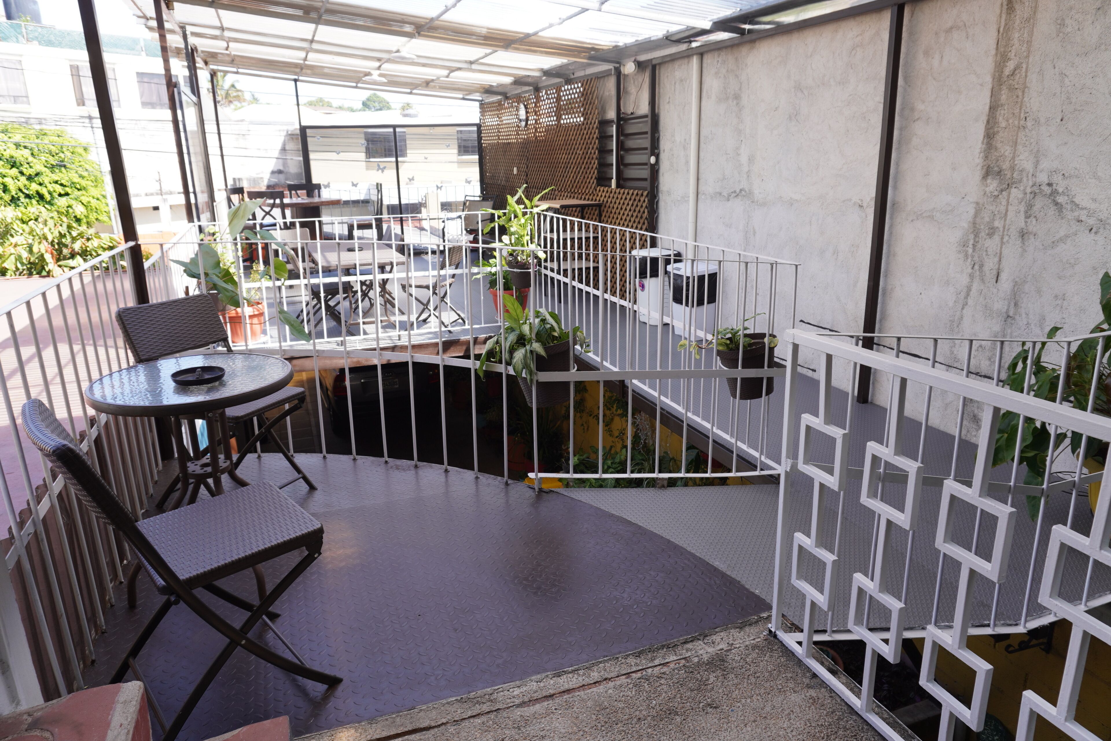Un espace extérieur abrité, aménagé avec une table ronde et des chaises, entouré de plantes en pot et d’une clôture en métal blanche.