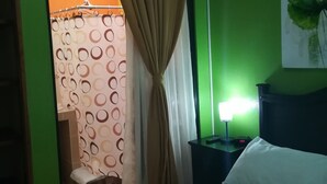 Ein Hotelzimmer mit Bett, Nachttisch mit Lampe, grüner Wand und Duschbereich.