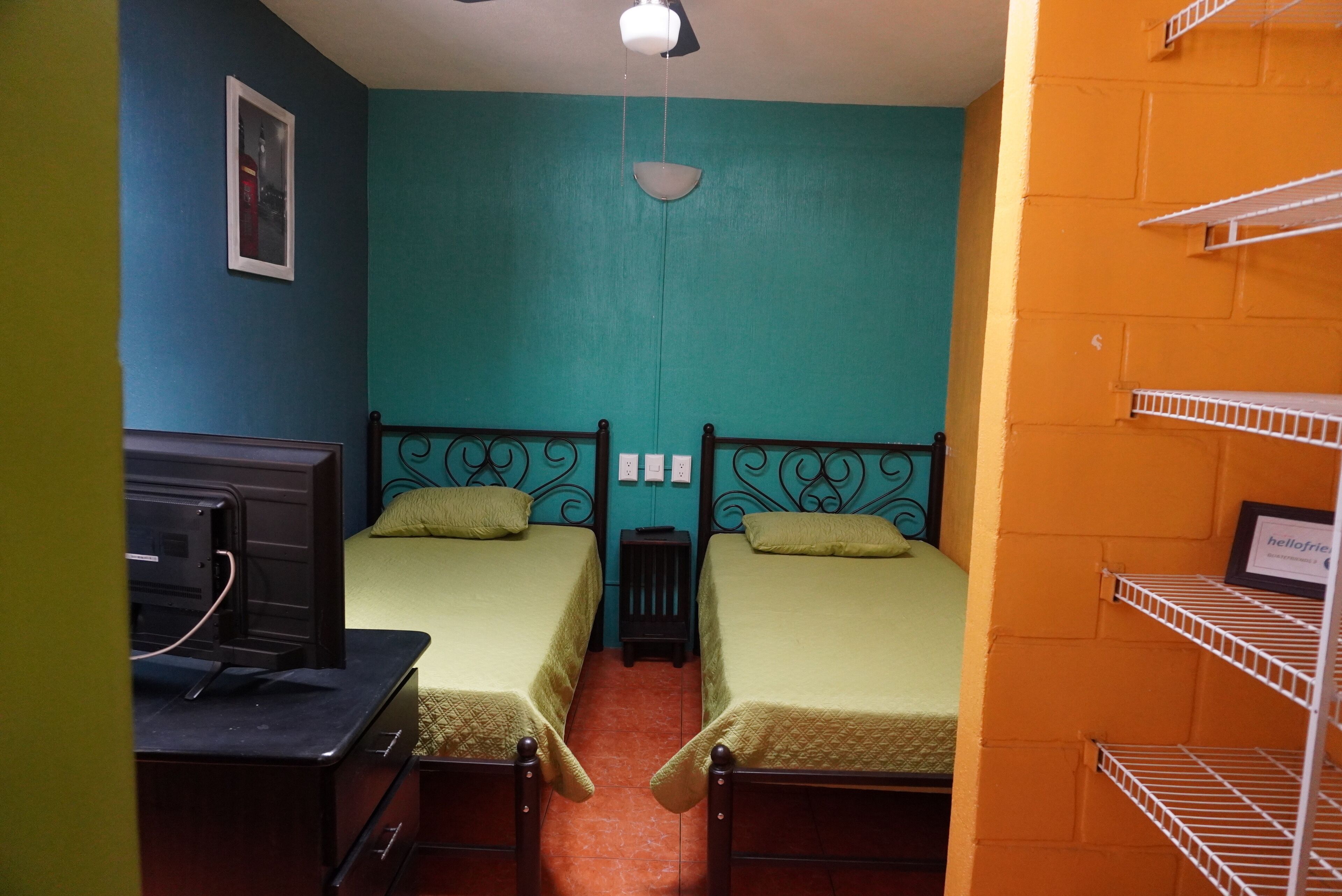 A room with two beds, a small table, a TV, and a shelf unit.