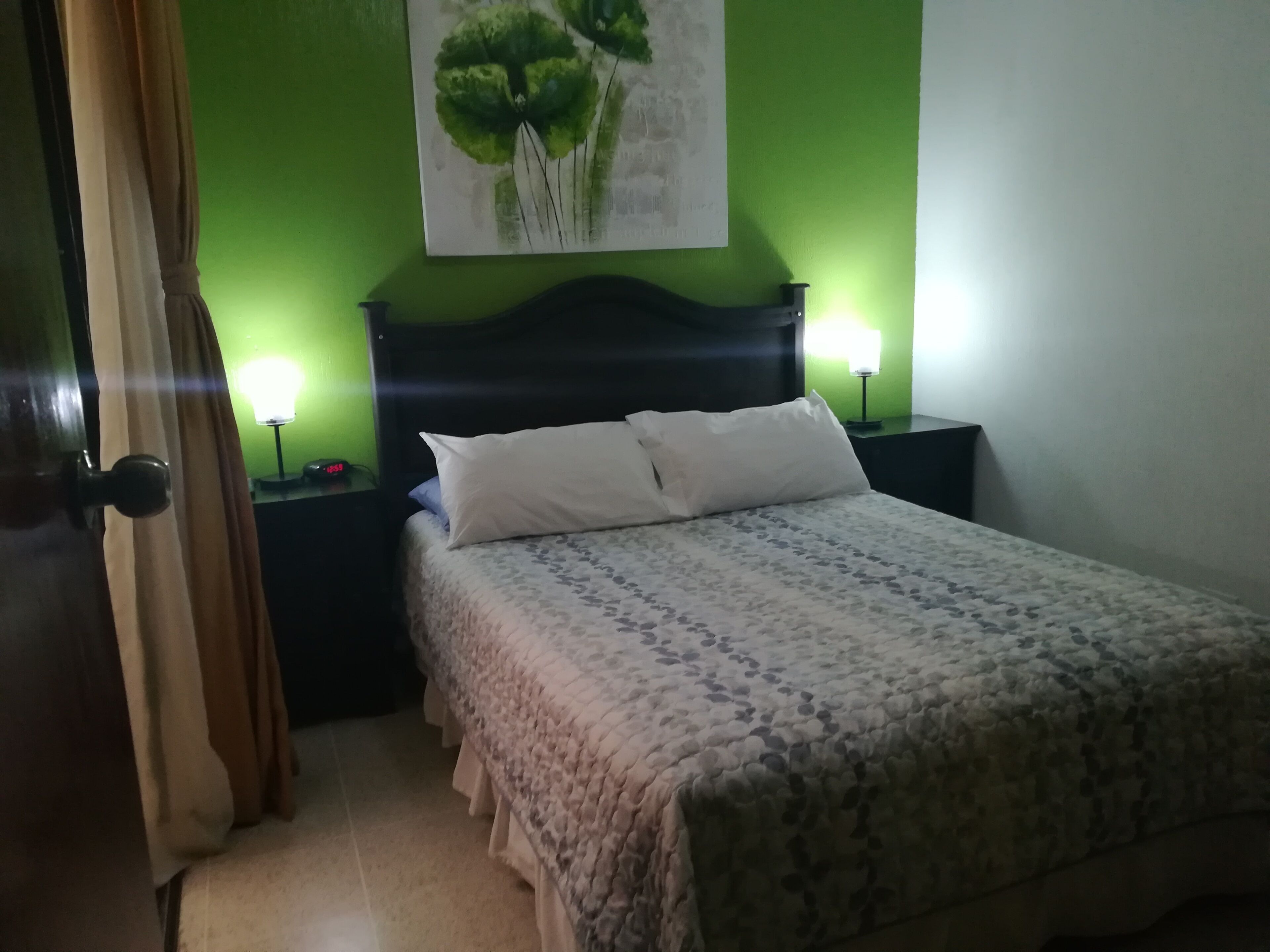 Una cama bien hecha con una colcha estampada y almohadas, un cabecero oscuro y dos lámparas de noche.
